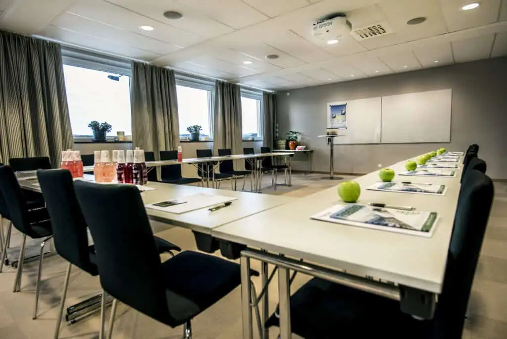 Främre bild av ett modernt konferensrum i Funäsdalen med stora fönster, gröna äpplen och konferensmaterial för effektiva fjällresor och fjällsemester.